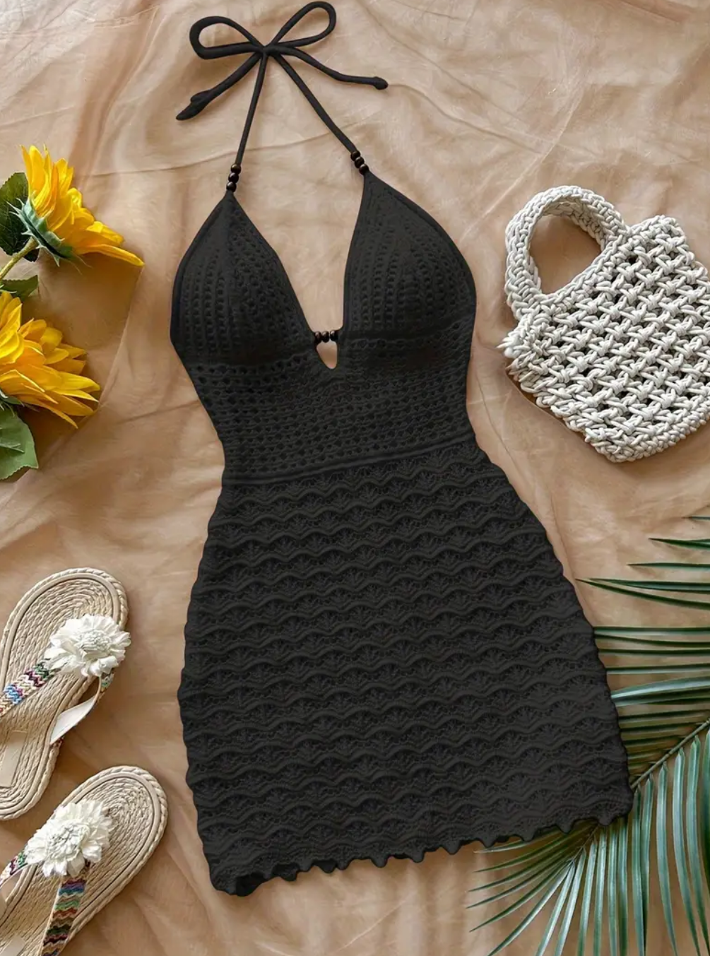 Black halter neck dress with a white woven bag and yellow flowers on a beige surface